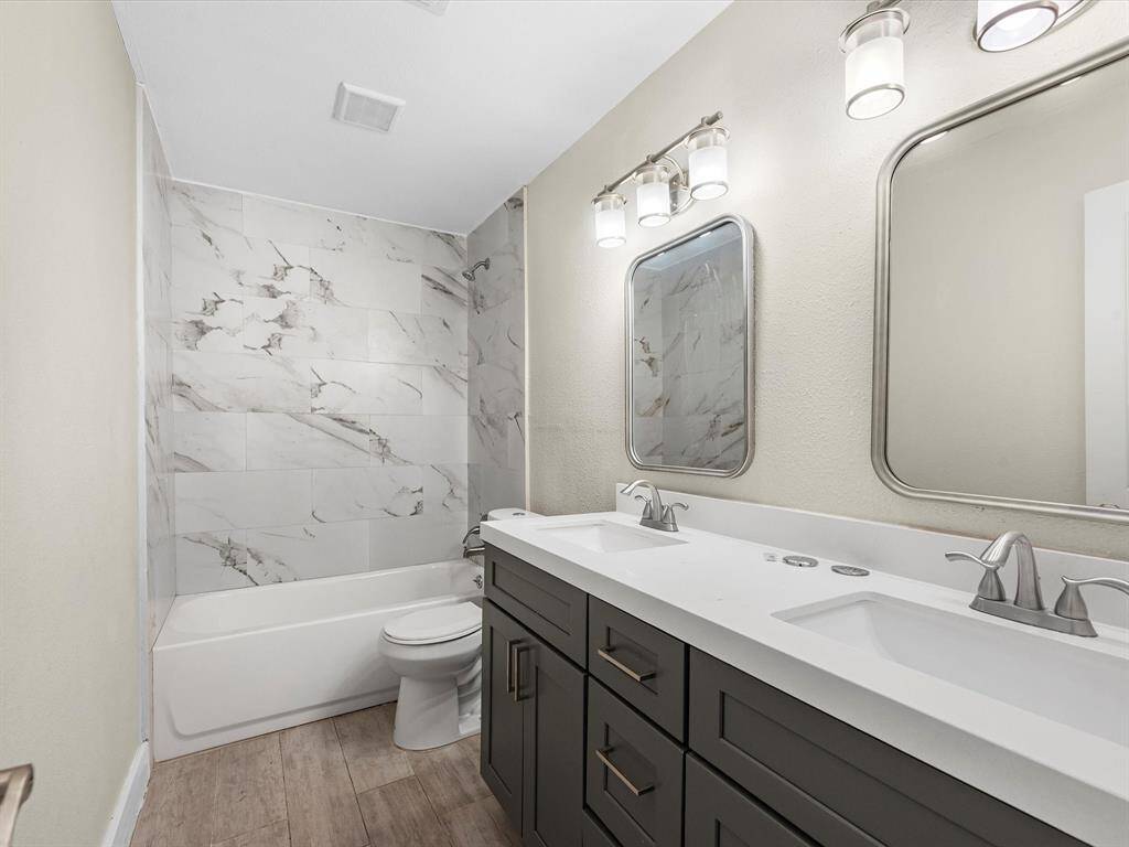 The hallway bathroom features a new vanity with double sinks, mirrors, and light fixtures, with stylish shower wall tiles, offering luxury and convenience to the secondary bedrooms.