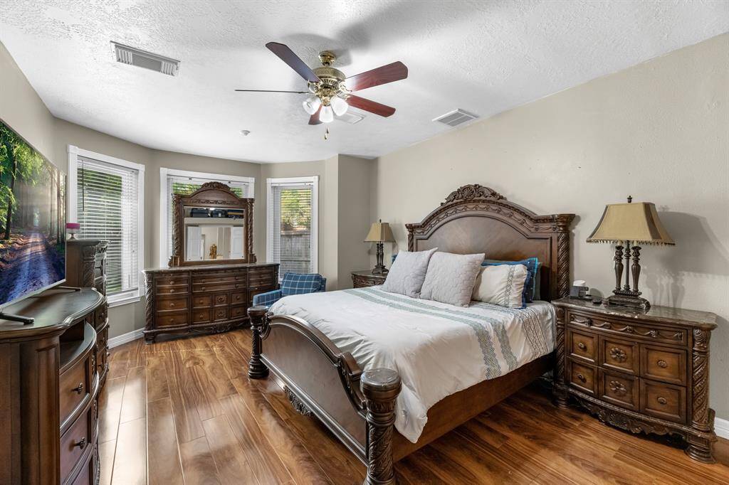 Discover comfort and elegance in this inviting bedroom featuring rich wood flooring, abundant natural light, and classic furnishings. Perfect for relaxation and style.