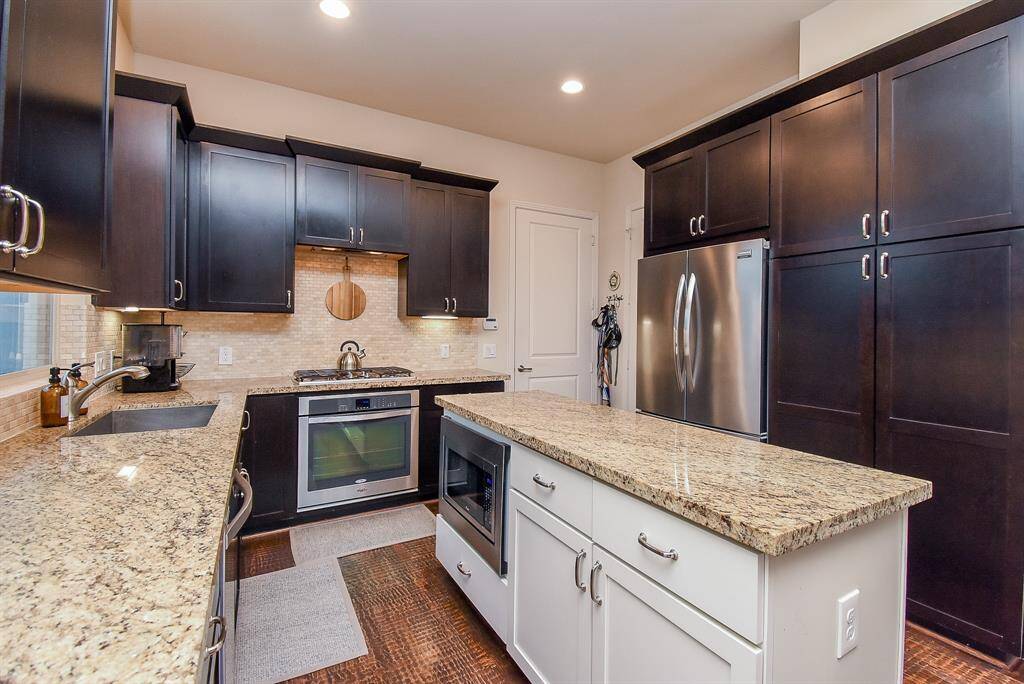 This winning dark/light dynamic is so rich and sophisticated in your large chef’s kitchen with creamy granite countertops, welcomed window over the sink and pale tile backsplash.  Note the double ovens just where you need them.