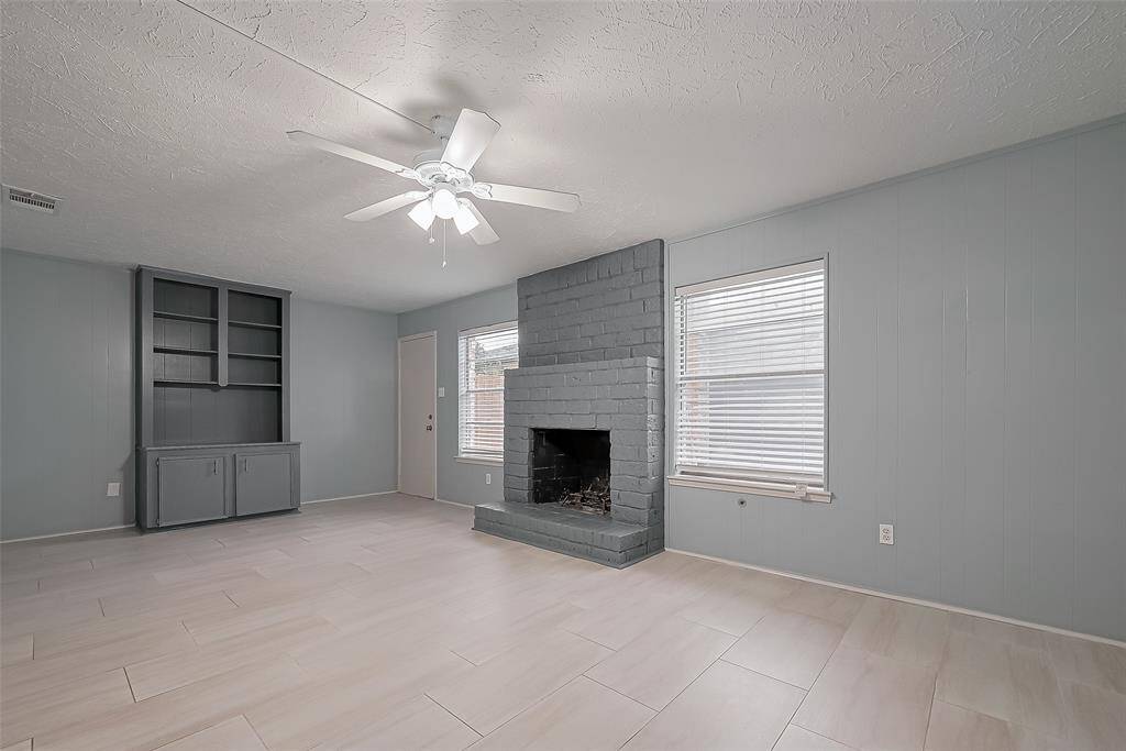 Anchored by a fireplace, this calming living space also features a ceiling fan, generous built-in shelving, and large windows that let in abundant light. Muted blue walls provide a soft, modern backdrop.