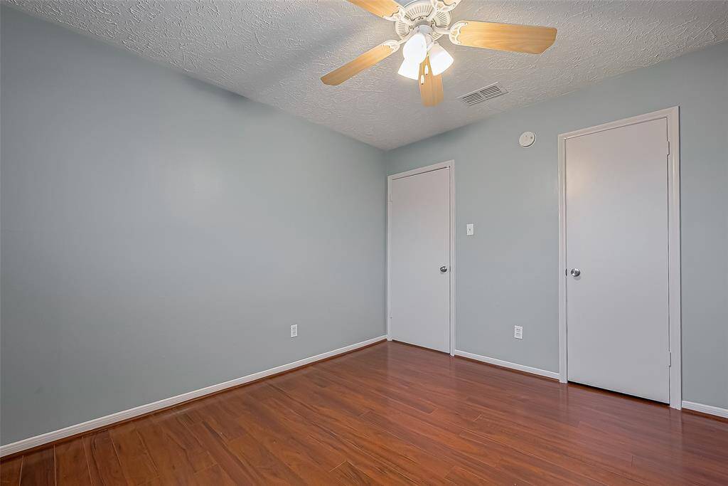 Soft blue walls and sleek laminate floors set a calming tone in this generous bedroom. Natural light pours through the wide window, and a ceiling fan tops it off.