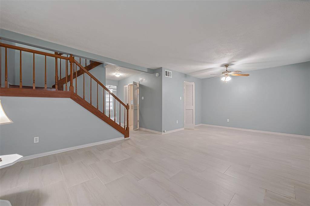 Nestled by the wooden staircase, this versatile space serves well as a sitting area or den. Tall windows, soft wall tones, and light flooring keep it bright yet cozy.
