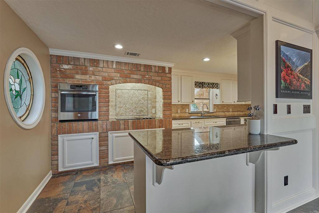 A charming stained glass window and exposed brick wall infuse the kitchen with character and warmth. The extended peninsula offers ample space for meal prep and casual seating, perfect for entertaining or everyday living.