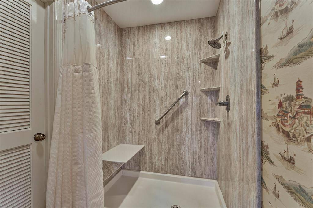 An updated shower features a built-in seat and shelving for convenient storage.