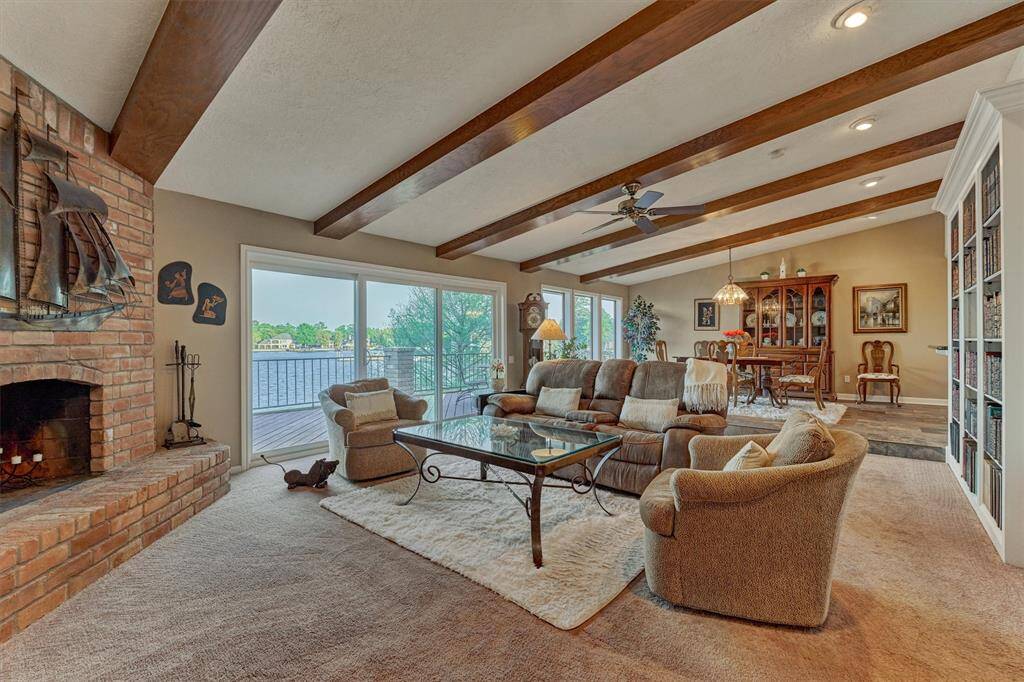 The living room features rustic wood beam accents and a charming corner brick fireplace. Large sliding glass doors and windows frame expansive views of Lake Conroe.