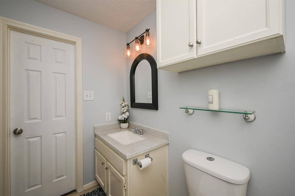 This bathroom features a modern vanity with a granite countertop, a stylish mirror, and contemporary lighting. Overhead cabinets for storage, and a sleek glass shelf. The neutral color palette creates a clean and inviting atmosphere.
