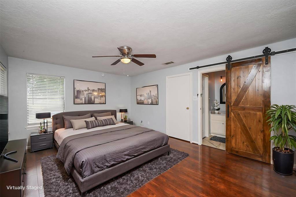 Spacious downstairs bedroom featuring elegant hardwood floors, a stylish sliding barn door, and abundant natural light.