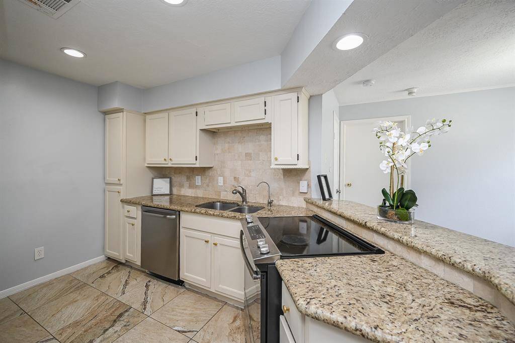This kitchen features elegant granite countertops, cream cabinetry, and modern stainless steel appliances. The open layout allows for natural light, and the neutral tile flooring complements the stylish backsplash.