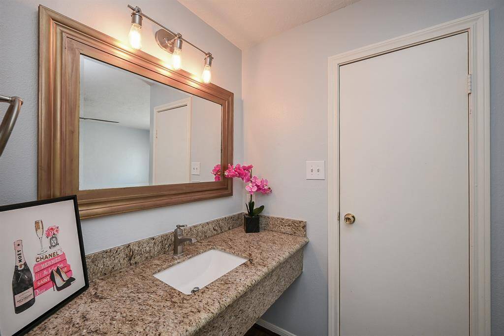 This bathroom features a stylish granite countertop with an under-mount sink, a large framed mirror, and modern lighting.