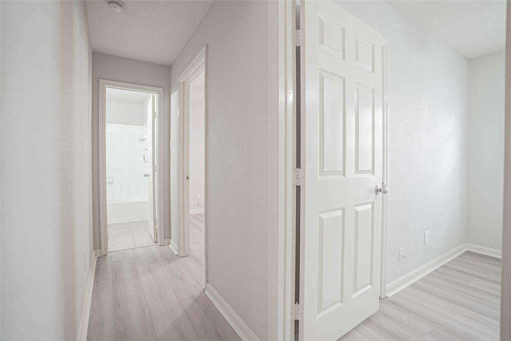 Bright, clean hallway with light wood flooring, leading to a bathroom with a tiled shower. Neutral wall colors and white doors create a fresh and inviting atmosphere.