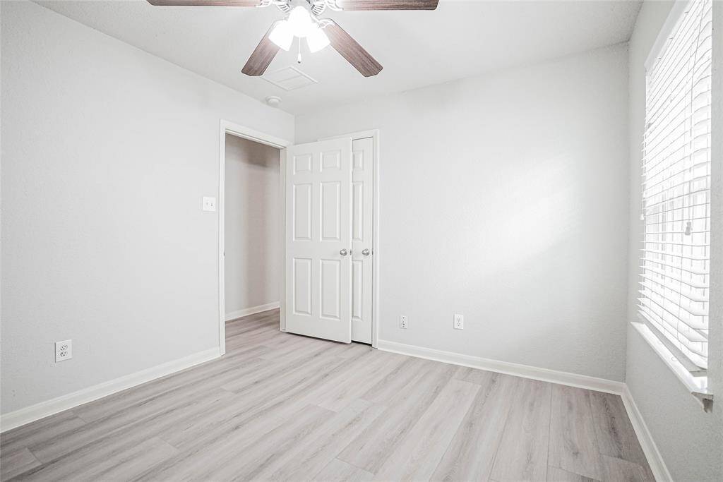 Bright, neutral-toned room with light wood flooring, a ceiling fan, and ample natural light from a window. Perfect for a bedroom or office space.