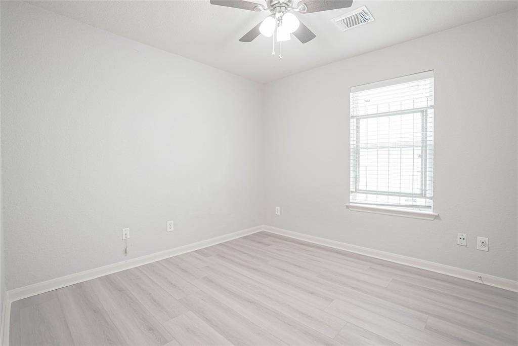 Bright and airy room with light gray walls and laminate flooring. Features a ceiling fan and a large window allowing natural light. Ideal for a bedroom or office space.