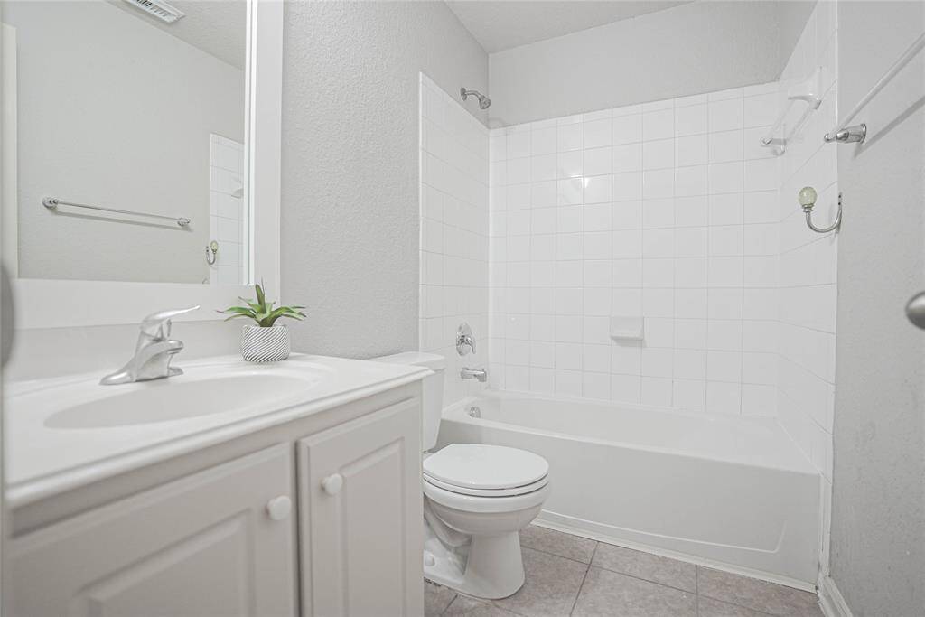 This is a bright, modern bathroom featuring a white vanity with a sink, a toilet, and a bathtub with a tiled shower area. The neutral color palette enhances its clean and fresh appearance.