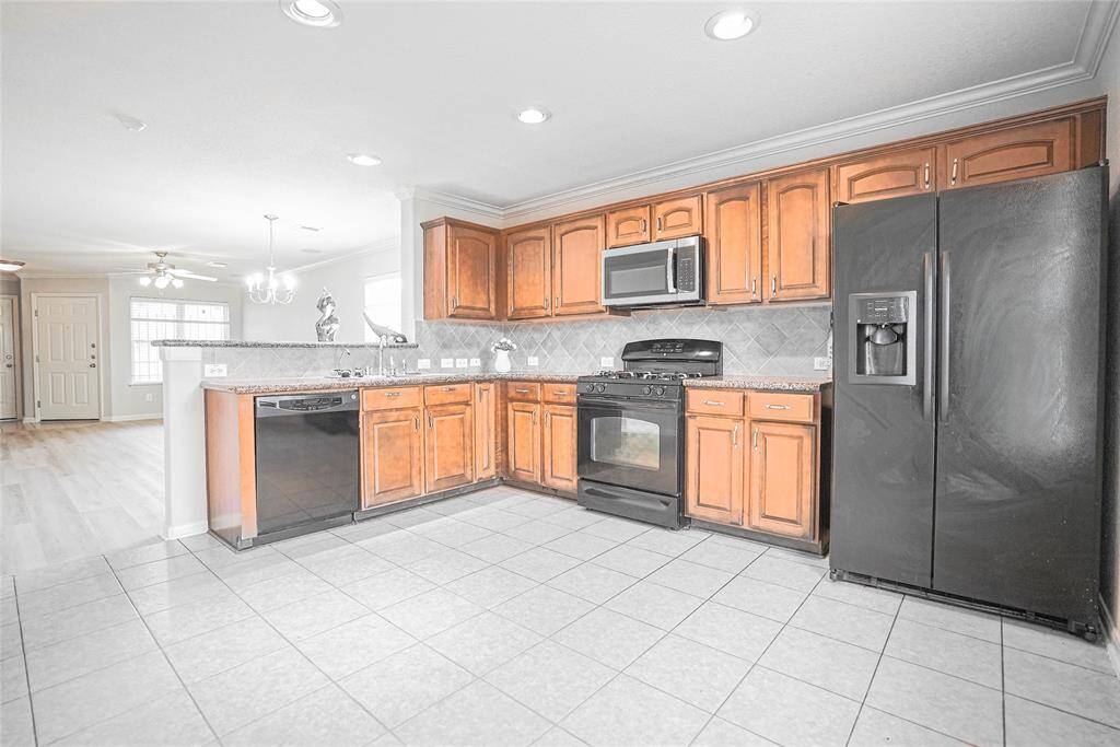 Spacious kitchen with modern appliances, wooden cabinets, and tile flooring. Open layout connects to a bright living area with hardwood floors, making it ideal for entertaining.