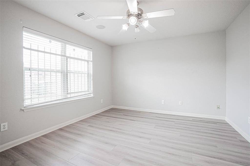 Bright and spacious room with light-colored laminate flooring, a large window with blinds, and a modern ceiling fan. Perfect for a bedroom or home office.