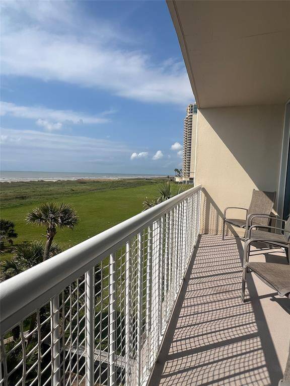 This photo shows a spacious balcony with seating, offering a scenic view of a lush green area and the ocean beyond. Ideal for enjoying serene coastal living.