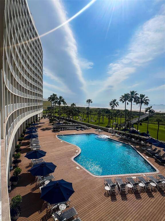 This photo showcases a beachfront property featuring a modern, curved building with balconies. The highlights include a spacious pool area with sun loungers and umbrellas, surrounded by palm trees, offering stunning ocean views. Perfect for those seeking a luxurious, resort-style living experience.