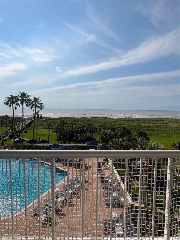 This photo showcases a stunning oceanfront view from a balcony, featuring a pool area with lounge chairs, lush greenery, and direct access to the beach via a boardwalk. Perfect for enjoying coastal living.