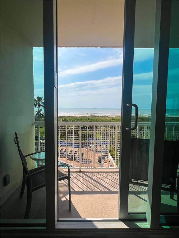 This photo shows a balcony view with glass doors opening to a scenic ocean panorama. The outdoor space includes a chair, offering a relaxing spot to enjoy the coastal landscape and blue skies.