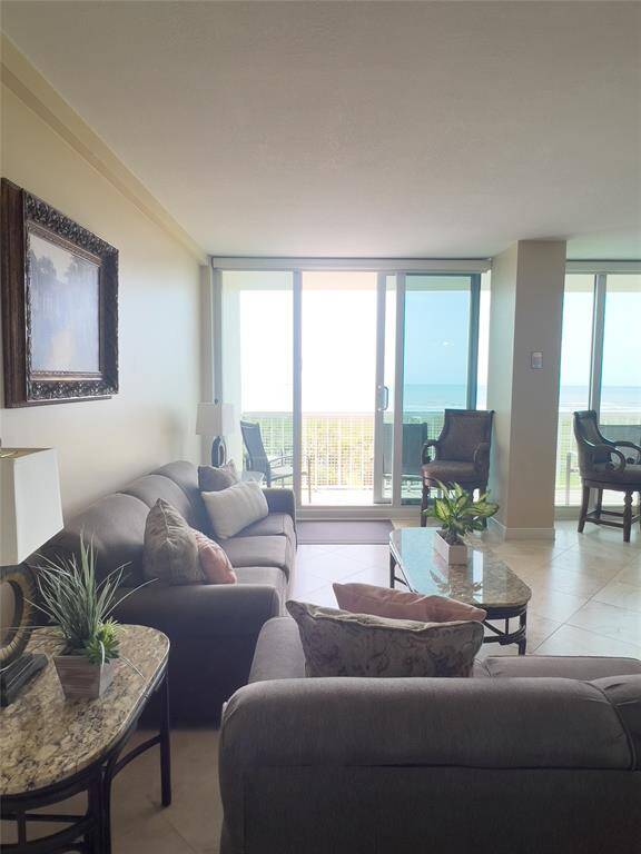 Bright living room with large glass doors leading to a balcony, offering stunning ocean views. Features comfortable seating, elegant decor, and natural light. Perfect for relaxation and entertaining.