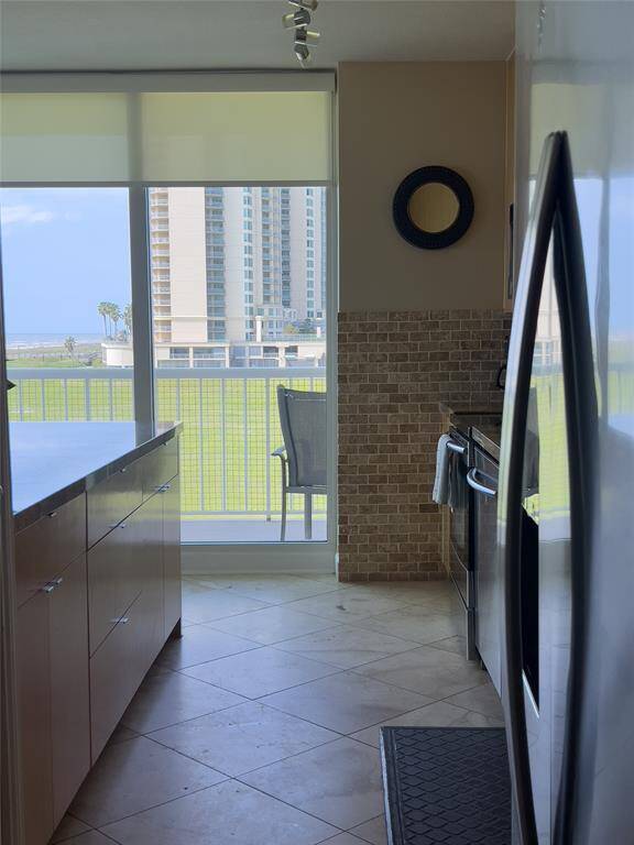 Modern kitchen with sleek cabinetry, stainless steel appliances, and tiled backsplash. Large windows provide ample natural light and offer a view of nearby buildings and greenery.
