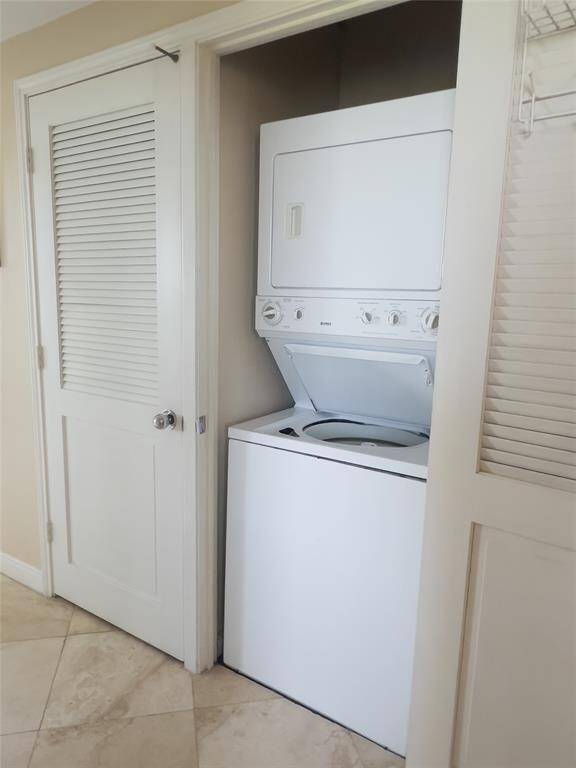 Compact laundry area with a white, stackable washer and dryer set in a closet with louvered doors. Neutral tile flooring complements the light walls.