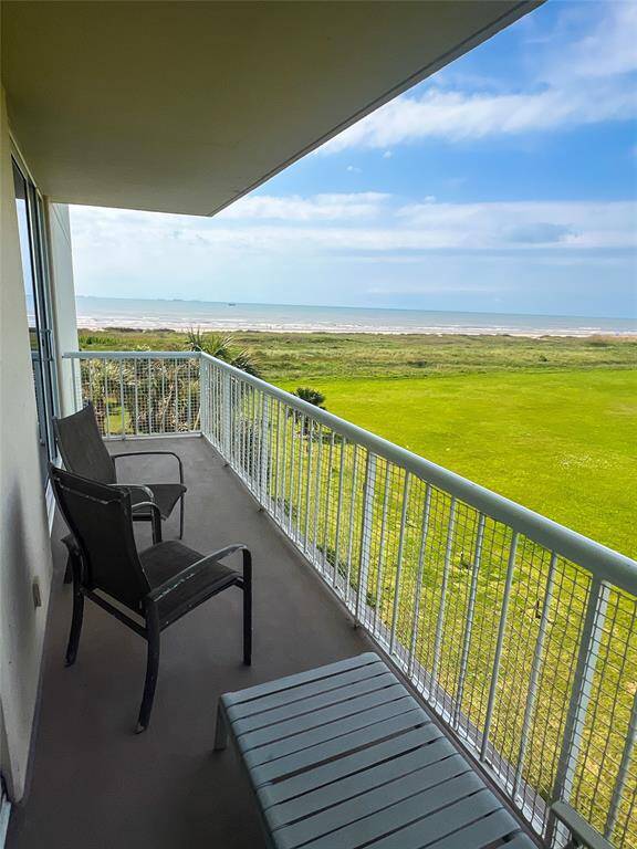 This photo showcases a spacious balcony with seating, offering stunning views of a green lawn leading to a beach and ocean, perfect for relaxation and enjoying coastal living.