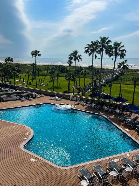 This photo showcases a property with a stunning beachfront view, featuring a large swimming pool surrounded by a wooden deck and lounge chairs. Palm trees and a boardwalk lead to the sandy beach, offering a serene coastal lifestyle.
