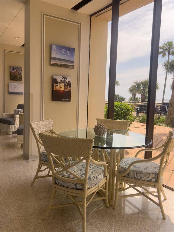 another view from the building lobby this bright and inviting space with wicker furniture and a glass-top table, set against large windows offering a view of palm trees and a deck outside. Perfect for enjoying natural light and outdoor scenery.