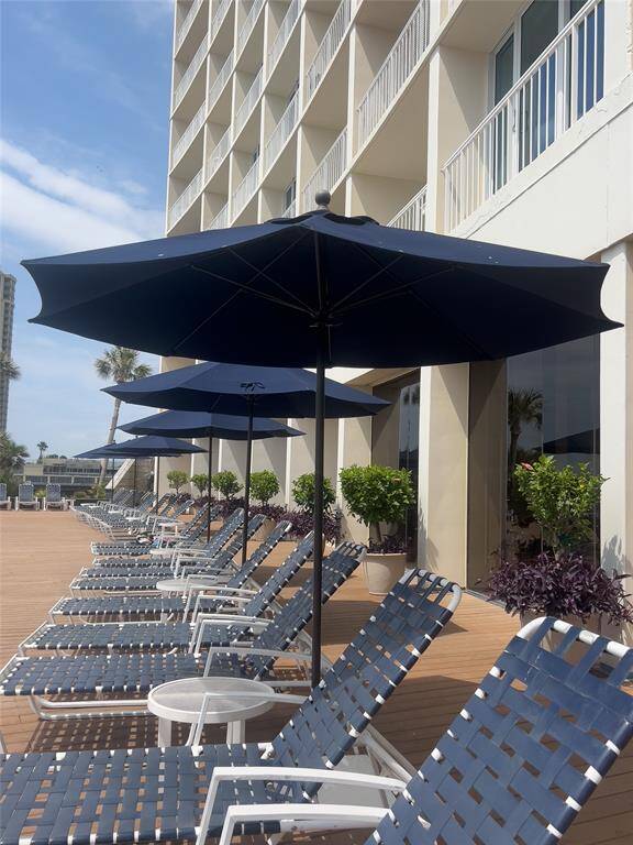 This photo showcases a sunny terrace with lounge chairs and umbrellas, perfect for relaxation. The area is adjacent to a modern building, ideal for enjoying outdoor leisure.