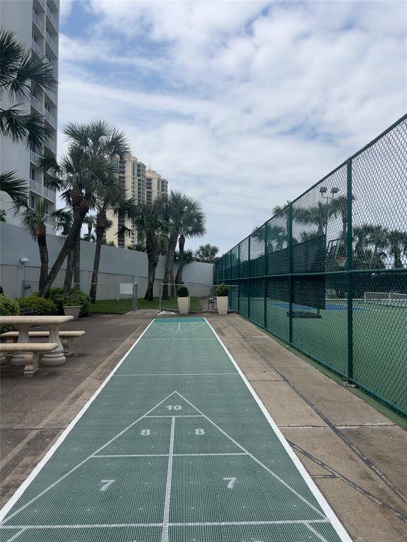 This photo features a recreational area with a shuffleboard court, adjacent to a tennis court, surrounded by palm trees and landscaping. It offers outdoor leisure activities in a well-maintained setting.