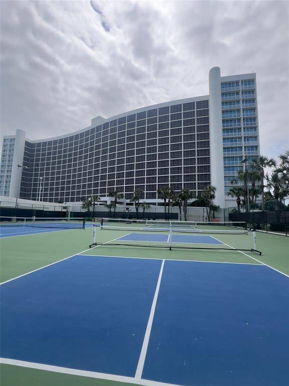 Modern high-rise building with a unique curved design, featuring adjacent tennis courts surrounded by palm trees, offering ample recreational space.
