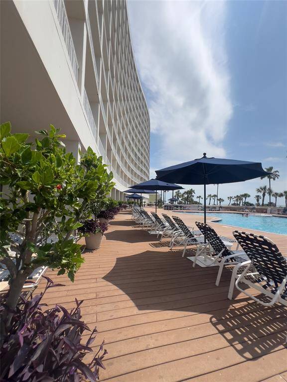 This photo showcases a modern condominium with a spacious pool deck featuring lounge chairs and umbrellas. The area is beautifully landscaped with greenery, offering a relaxing outdoor environment ideal for leisure and entertainment.
