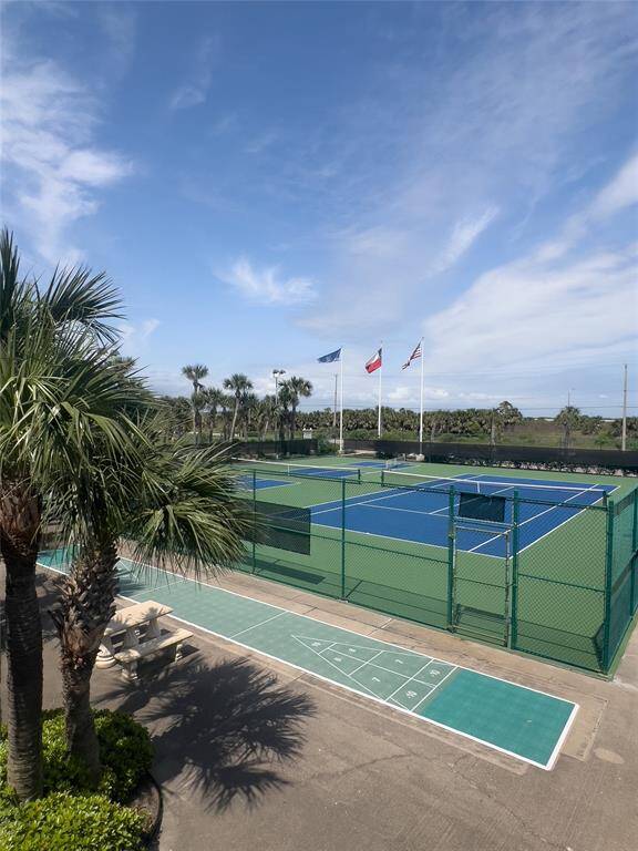 This property features a well-maintained tennis court and shuffleboard area, surrounded by lush palm trees, offering a sporty outdoor lifestyle under clear blue skies.
