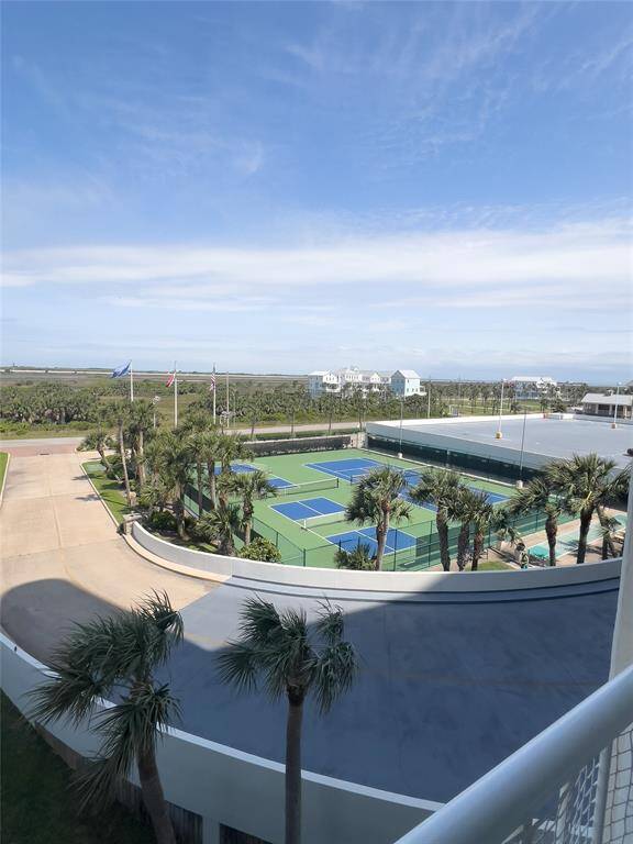 This photo showcases a view from a balcony overlooking tennis courts surrounded by palm trees, with a clear sky and neighboring houses in the distance. Ideal for those seeking a home with recreational amenities and scenic views.
