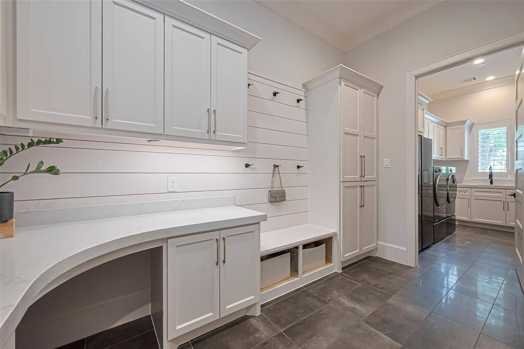 This ideal mudroom is spacious and designed for ample storage with built-in shelves and cabinets, featuring a convenient desk located near the kitchen. The utility room is situated at the back for added functionality.