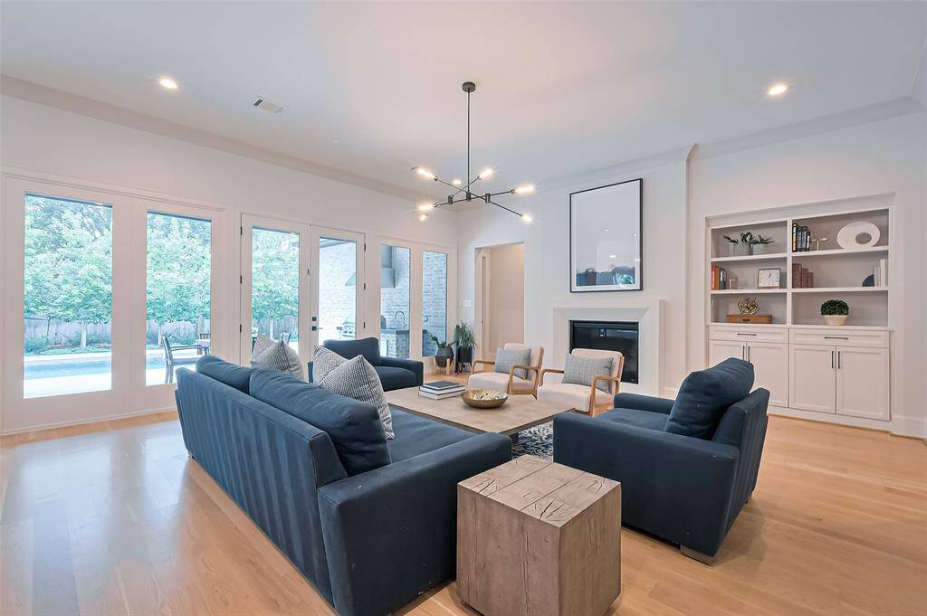 The formal living room is illuminated by warm, natural light, creating a welcoming and inviting atmosphere. It features built-in shelves, a modern gas log fireplace, and doors that lead out to the patio and private backyard. Desirable open-concept layout, perfect for today's lifestyle and entertaining. All chandeliers will remain with the home.