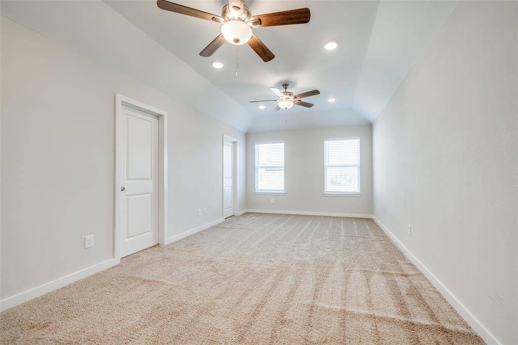 Bright primary bedroom with ceiling fan and fresh carpet.