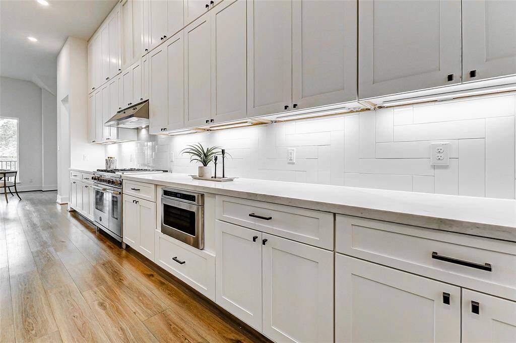 Wow, just look at the abundant storage in this kitchen! The crisp white cabinetry creates a clean, modern aesthetic, complemented by a thoughtful mix of drawers and cabinets. Under-cabinet lighting highlights the stylish designer backsplash, while the microwave is seamlessly integrated into the cabinetry for added convenience and sleek design.