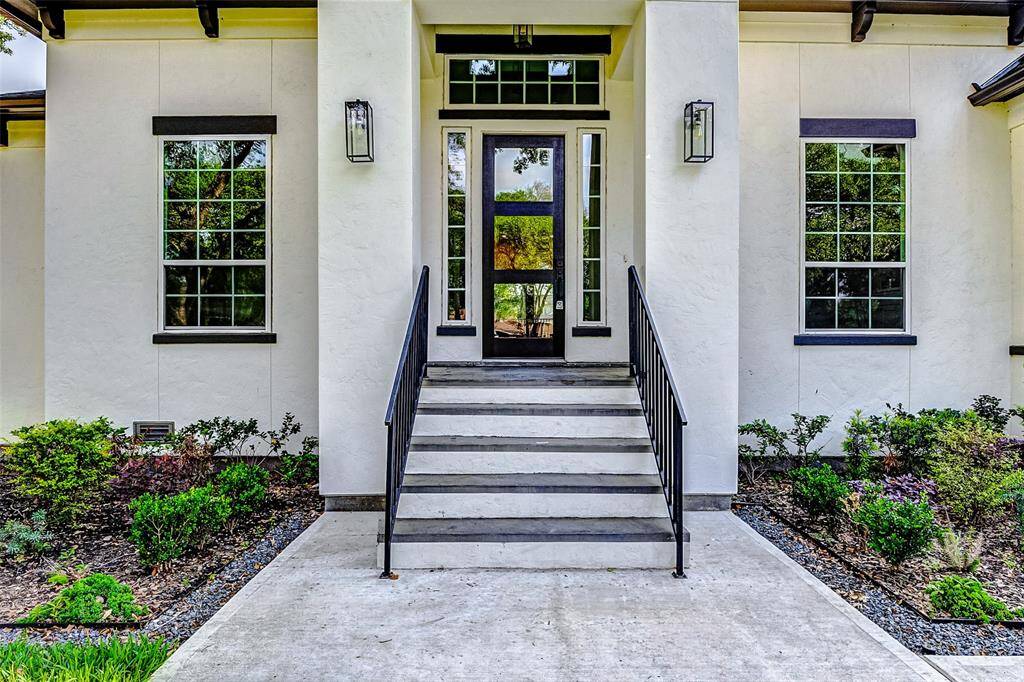 Graceful wrought iron railings frame the front steps, leading to an inviting covered porch. The front door, adorned with elegant glass inserts and flanked by transom and sidelight windows, fills the entryway with abundant natural light and charm.