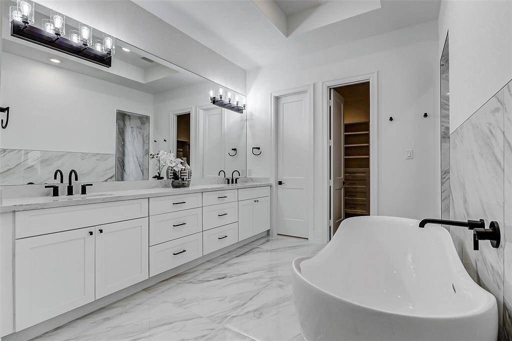 What a stunning en suite bathroom! This serene retreat features dual vanities with crisp white cabinetry and coordinating countertops, complemented by oil-rubbed bronze fixtures. A large frameless mirror, vanity lighting, and an oversized walk-in shower add to the sense of luxury. The space also includes a deep soaking tub, a linen closet for added convenience, and a privately tucked-away commode for ultimate privacy.