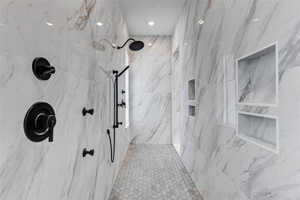 The expansive walk-in shower offers a spa-like experience, featuring dual shower heads, a body spray, and multiple built-in niches for convenience. The stunning marble-look tile surround, upgraded tile flooring, and thoughtful lighting—window and recessed disk lights—combine to create a luxurious, tranquil retreat.