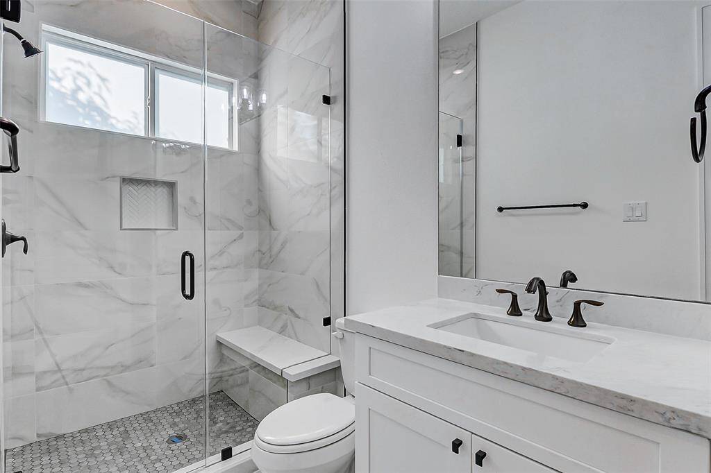 This secondary bathroom features a luxurious walk-in shower, highlighted by a custom frameless glass enclosure and a convenient bench seat. A privacy window allows natural light to fill the space, enhancing both the functionality and the serene atmosphere.