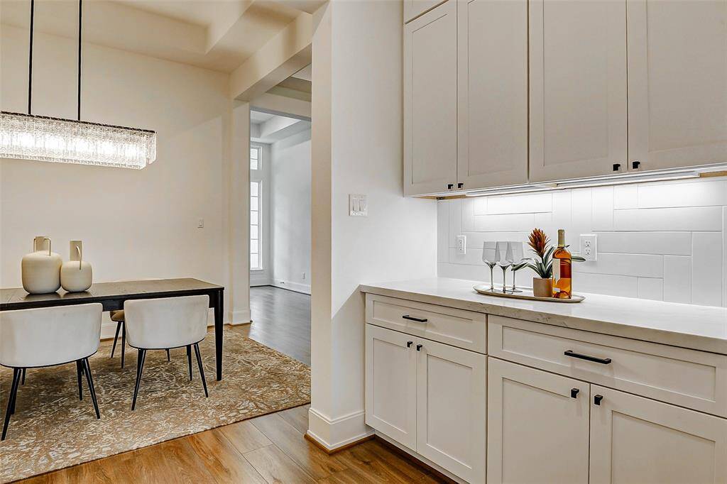 Just beyond the dining room, a beautifully appointed dry bar awaits—featuring crisp white cabinetry, sleek quartz countertops, and soft under-cabinet lighting that adds both function and ambiance. A perfect touch for effortless entertaining.