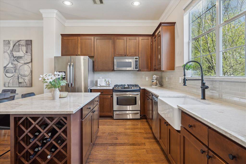 Bright and beautiful kitchen featuring Taj Mahal Quartzite countertops, a farmhouse sink, and a fresh tile backsplash—all illuminated by a large window!