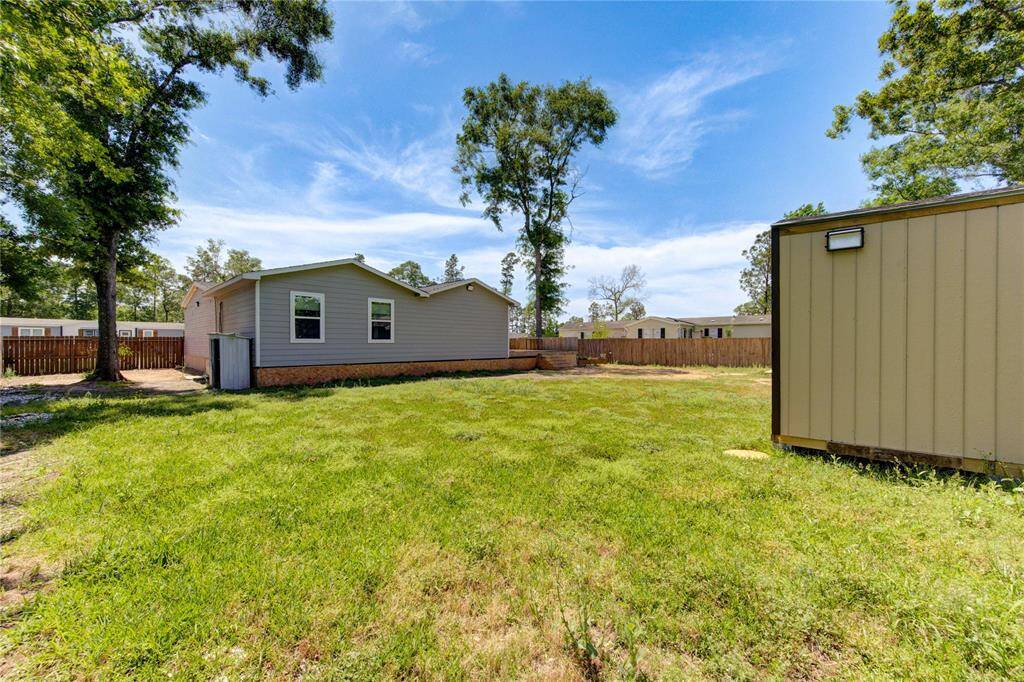 Spacious backyard with a well-maintained lawn, surrounded by a wooden fence for privacy. The area includes a storage shed and features a single-story home with light siding and multiple windows, providing a serene outdoor space.