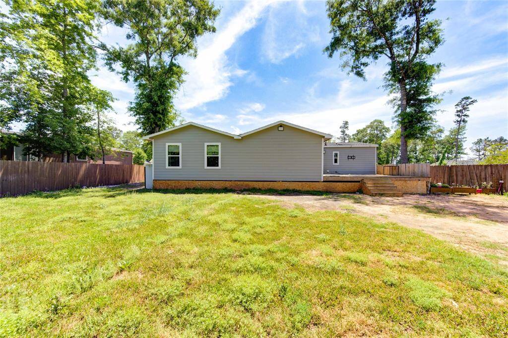 This photo shows a single-story home with a spacious backyard, surrounded by a wooden fence and mature trees, offering privacy and a natural setting. The exterior is simple and well-maintained, featuring a small deck with steps.