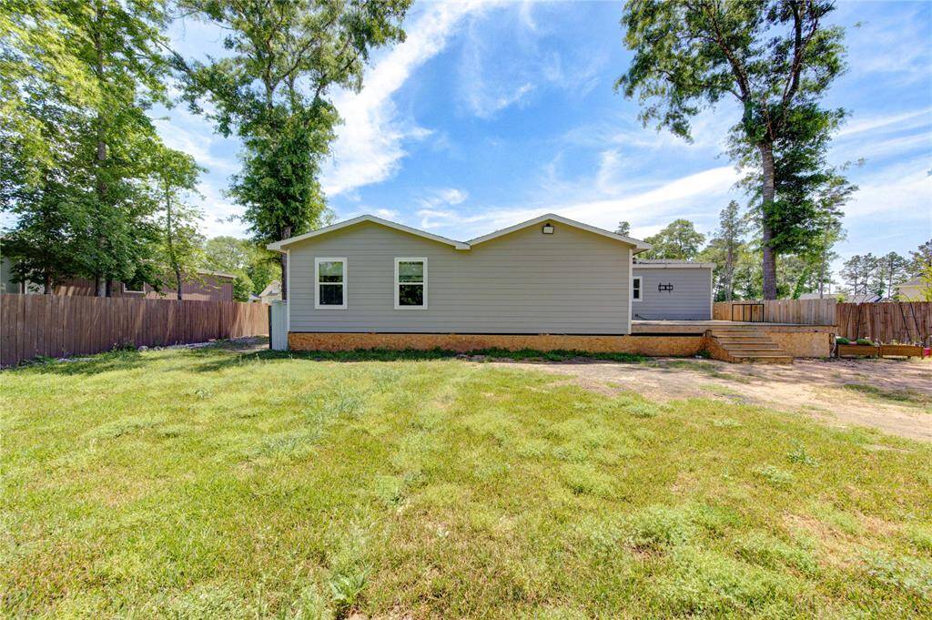 This photo showcases the rear view of a house featuring a spacious, grassy backyard with a wooden fence and mature trees, ideal for outdoor activities and privacy. The home has a simple, single-story design with a small deck area.