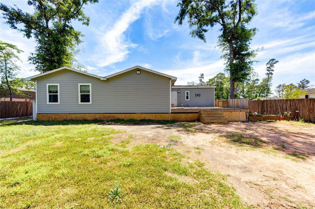 This property features a single-story home with a light gray exterior and a spacious backyard. It includes a raised wooden deck with steps, surrounded by a wooden fence for privacy. The yard offers ample space for gardening or outdoor activities, with mature trees providing natural shade.