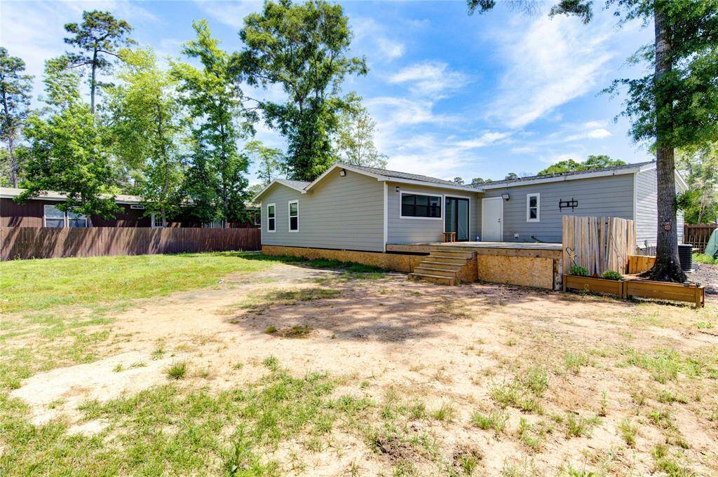 This photo showcases a single-story home with a spacious backyard, featuring a wooden deck and surrounded by a mix of grass and dirt. Tall trees and a wooden fence provide privacy and a natural setting.